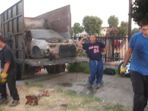 1991 Ford Taurus - A severely damaged car is being loaded onto a flatbed truck, with two men nearby.