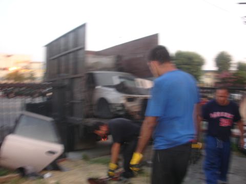 1991 Ford Taurus - Junkyard scene with people and discarded vehicle parts.