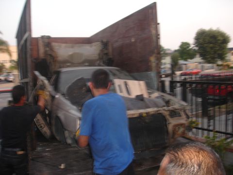 1991 Ford Taurus - Two men load a heavily damaged car onto a truck bed, with the front of the vehicle visible.