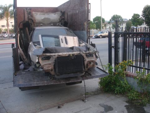 1991 Ford Taurus - A heavily damaged car is loaded onto a flatbed truck, its front end completely destroyed.