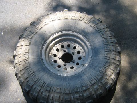 1990 Ford Bronco - A close-up view of a off-road tire mounted on a metal wheel, resting on pavement.