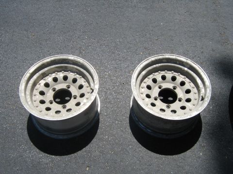 1990 Ford Bronco - Two aluminum alloy wheels are shown resting on a dark asphalt surface.