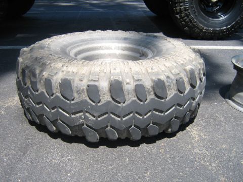 1990 Ford Bronco - A single tire with a worn, aggressive tread pattern sits on a paved surface.