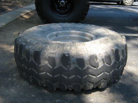 1990 Ford Bronco - A large off-road tire is shown on the ground, with part of another vehicle in the background.