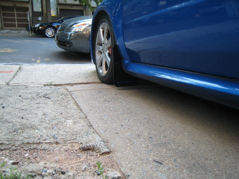 2007 Subaru Impreza - Mudflaps are visible on the side of a blue car parked on a street.