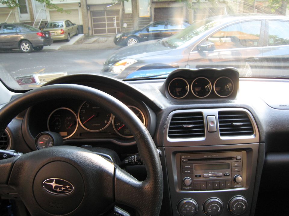 Interior shot of a 2007 Subaru Impreza, showing the steering wheel, dashboard gauges, and triple pod gauges on top of the dash