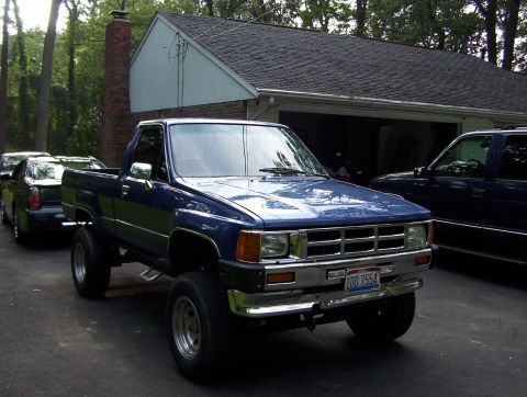 1986 Toyota Hilux - This blue pickup truck is parked in front of a garage with other vehicles nearby.