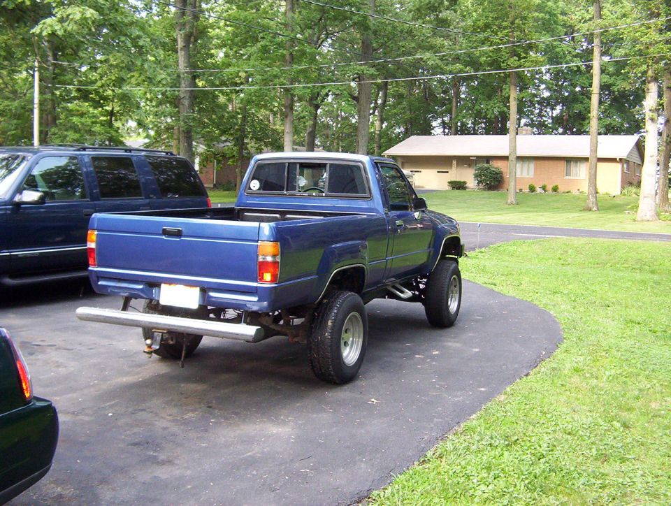 1986 Toyota Hilux pickup truck parked in driveway, rear view. Another SUV is parked to the left