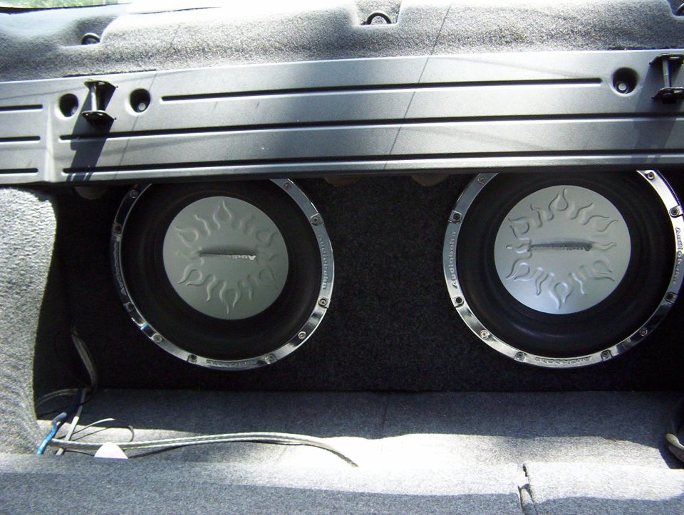 Two car subwoofers mounted in a trunk, with silver cones and flame designs
