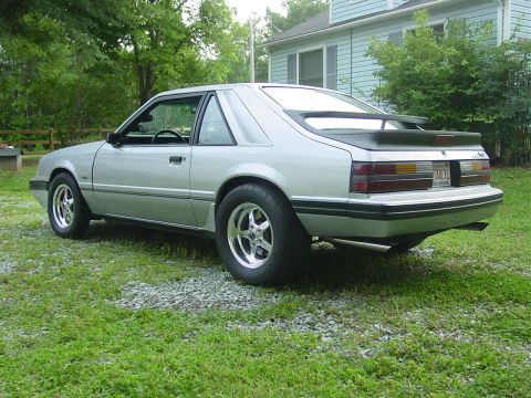 1986 Ford Mustang - A silver 1986 Ford Mustang coupe is parked on a grassy area with a house in the background.