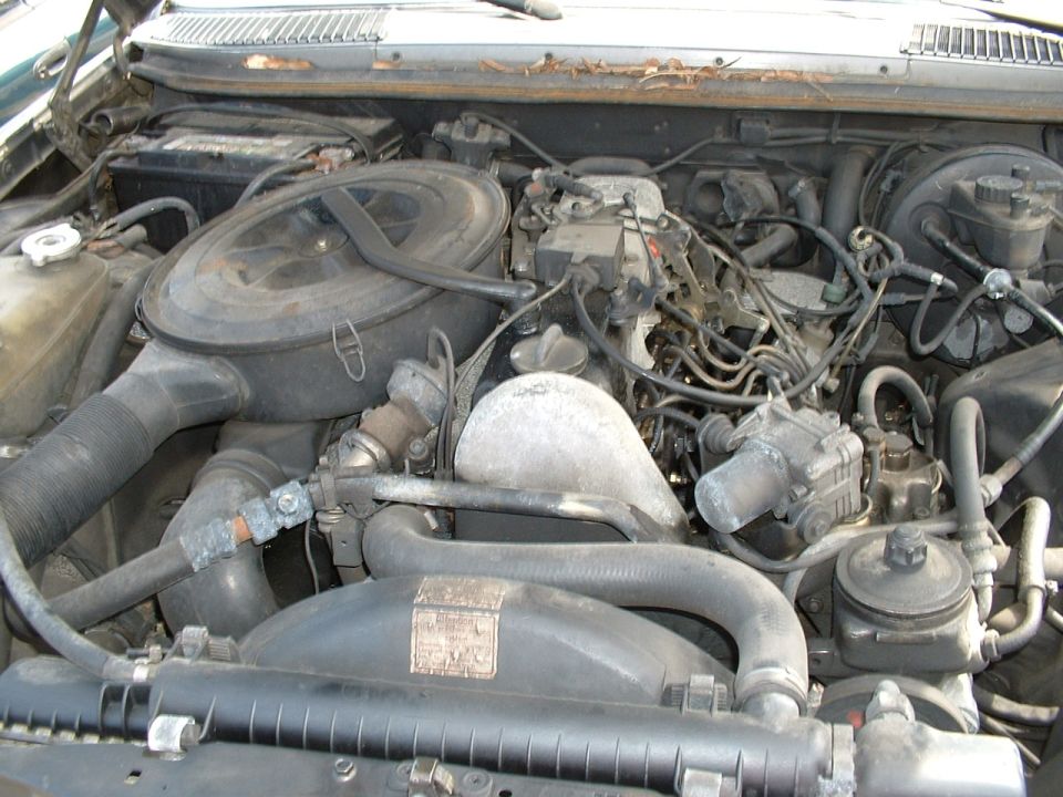 Dusty engine bay of a Mercedes-Benz diesel with round air cleaner, hoses, and injection lines