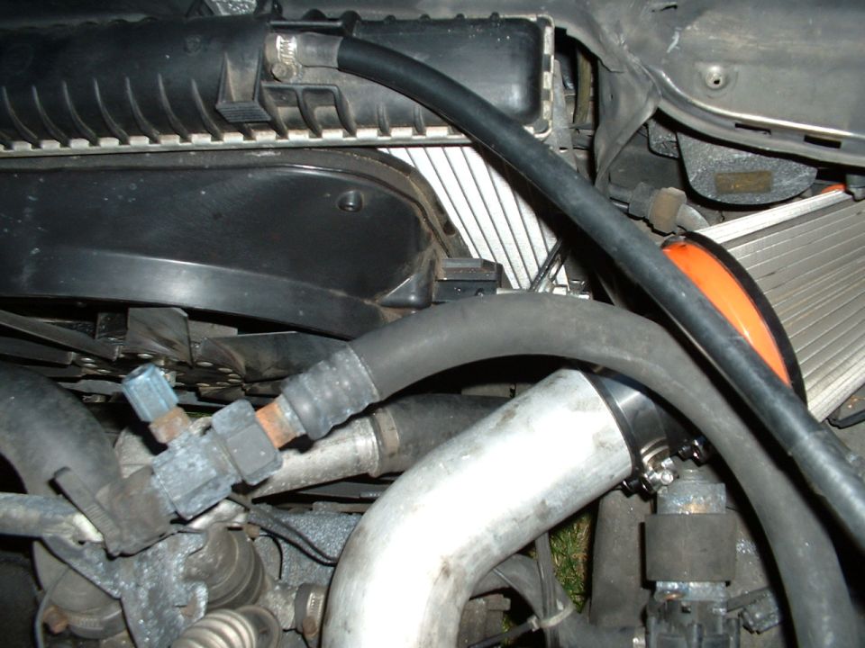 Engine bay close-up with radiator, black hoses, aluminum pipe with clamp, and orange duct hose