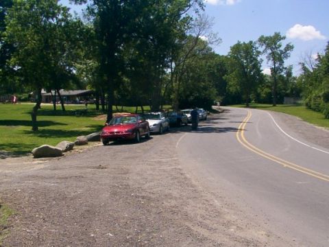 1998 Ford Taurus - A red 1998 Ford Taurus is parked on a gravel shoulder next to a winding road, with other vehicles visible in the background.