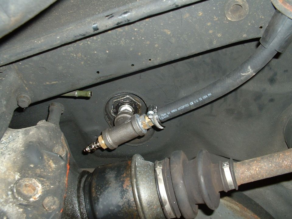 Underbody photo of a fuel hose with clamp attached to a fitting through the floor, CV axle boot below