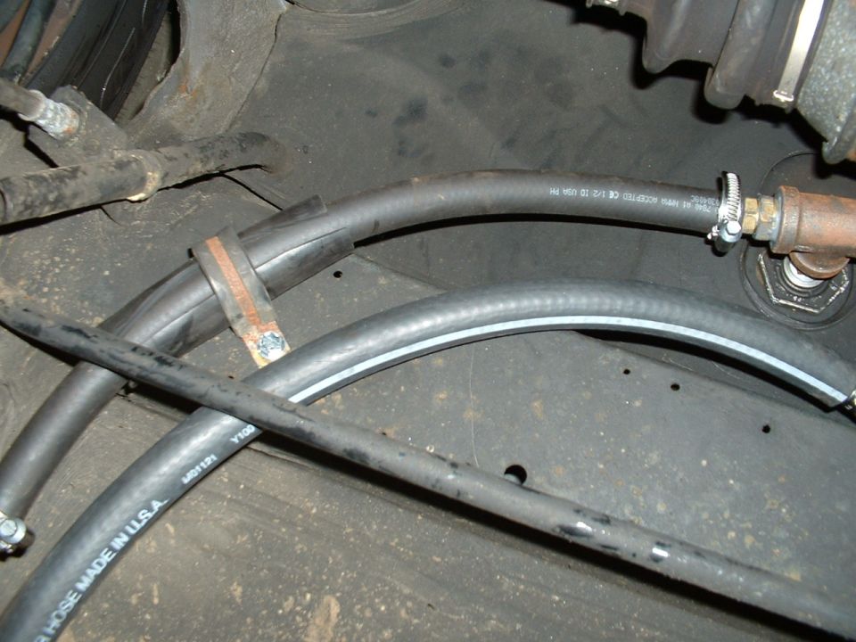 Underbody view of rubber hoses with clamps and brass fitting beneath a vehicle
