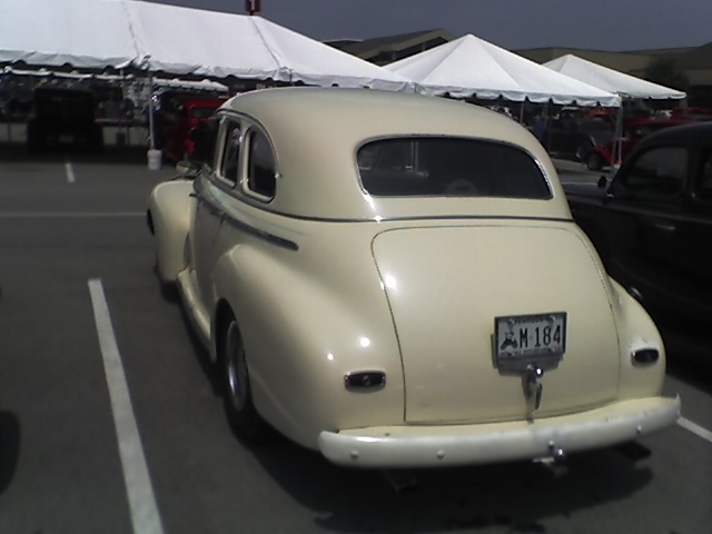 Rear view of a cream-colored vintage sedan with a license plate reading M 184