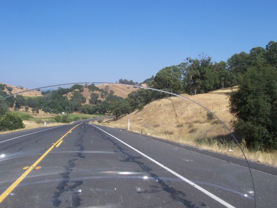 View from car on highway with rolling hills and trees under a clear blue sky