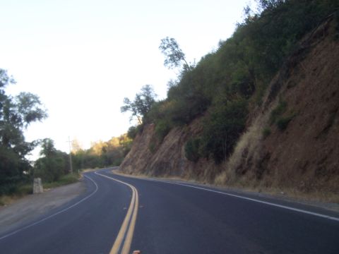 1994 Ford F-150 - A two-lane road curves through a landscape with a steep, vegetated embankment on the right and trees on the left.