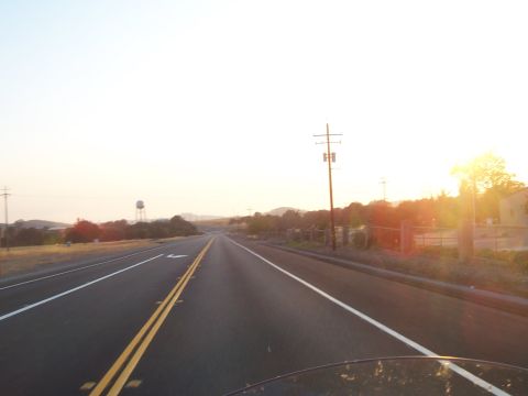 1994 Ford F-150 - A long, empty highway stretches towards the horizon under a bright, hazy sky at sunset.
