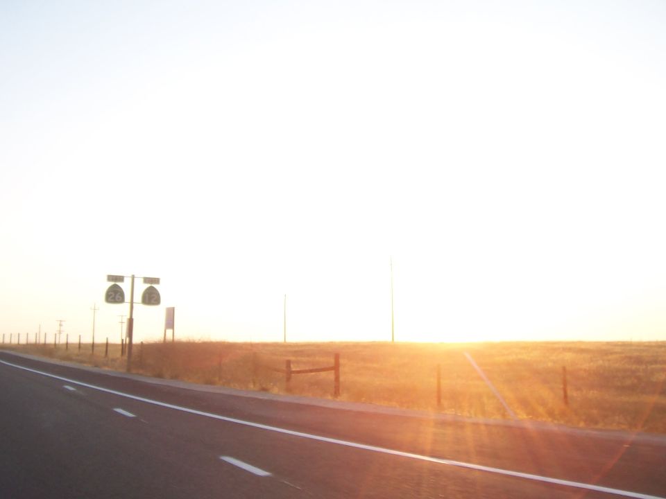 Roadside signs with numbers 26 and 12 under a bright sunset