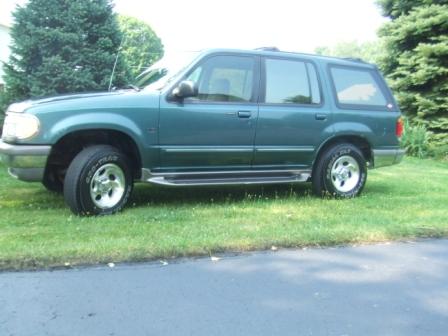1996 Ford Bronco - This green SUV is parked on a grassy area next to a paved surface, with trees in the background.