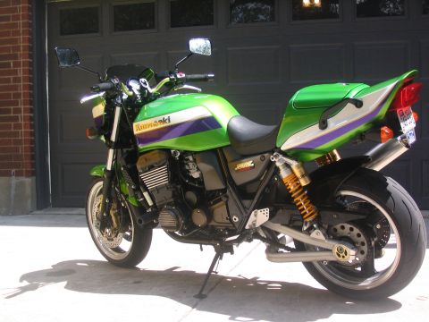 1981 Kawasaki Bayou - A green Kawasaki motorcycle with distinctive purple and white racing stripes is parked outside a garage.