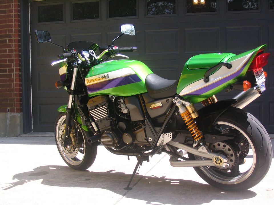 Green Kawasaki motorcycle parked in front of a garage door. It has purple and white stripes on the tank and tail