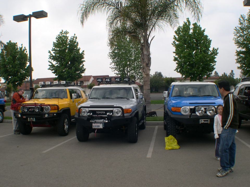 Three Toyota FJ Cruisers parked in a lot, one yellow, one silver, one blue