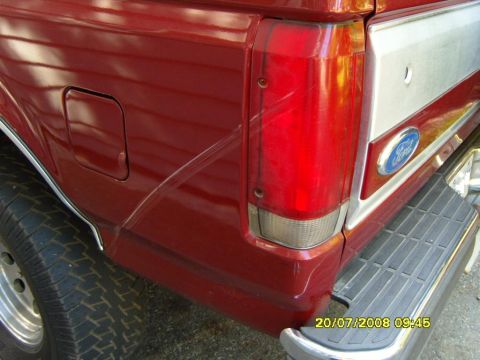 1989 Ford Bronco - Close-up rear view of a red 1989 Ford Bronco showing the taillight, fuel door, and part of the chrome bumper. A silver stripe runs along th…