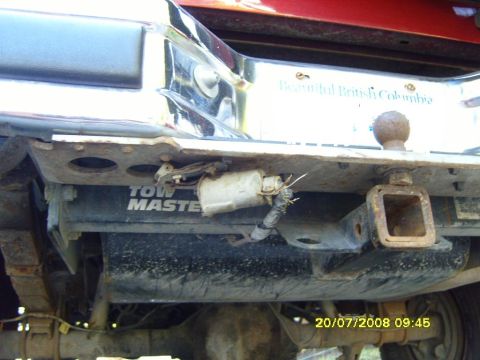 1989 Ford Bronco - The rear underside of a vehicle shows a rusty trailer hitch receiver and a "TOW MASTER" branded component. A license plate frame that reads…
