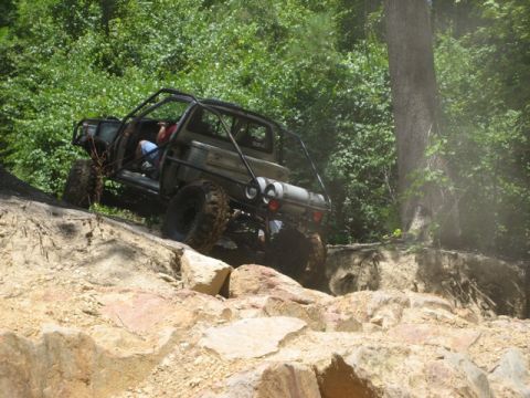 1995 Ford Bronco - This heavily modified off-road vehicle navigates a steep, rocky incline surrounded by dense foliage.