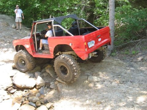 1995 Ford Bronco - This red Ford Bronco is tackling a challenging off-road trail with large tires.