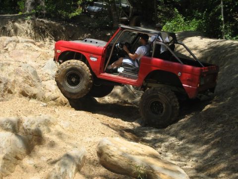 1995 Ford Bronco - A red off-road SUV tackles a challenging rocky trail with a second vehicle visible in the background.