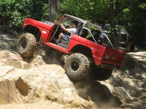 1995 Ford Bronco - A red SUV navigates a challenging rocky terrain with a second vehicle visible in the background.