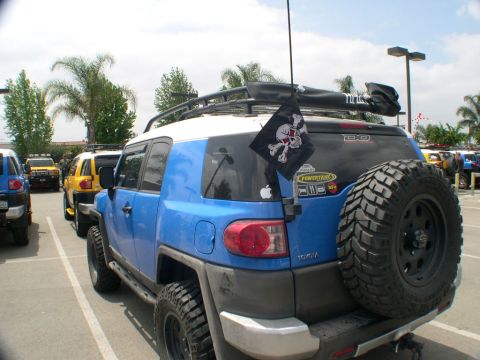 2007 Toyota FJ Cruiser - A blue 2007 Toyota FJ Cruiser is parked with other vehicles, displaying a pirate flag and a spare tire mounted on the back.