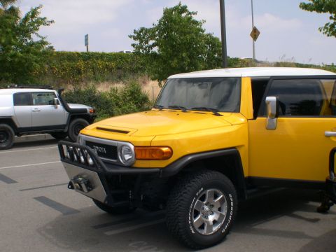 2007 Toyota FJ Cruiser - Two Toyota FJ Cruisers, one yellow and one silver, parked in a lot.