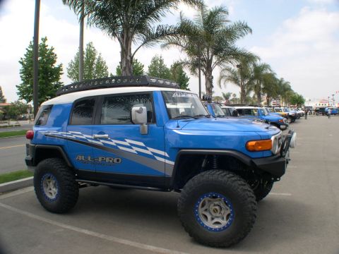 2007 Toyota FJ Cruiser - A line of Toyota FJ Cruisers are parked under palm trees at an outdoor event.