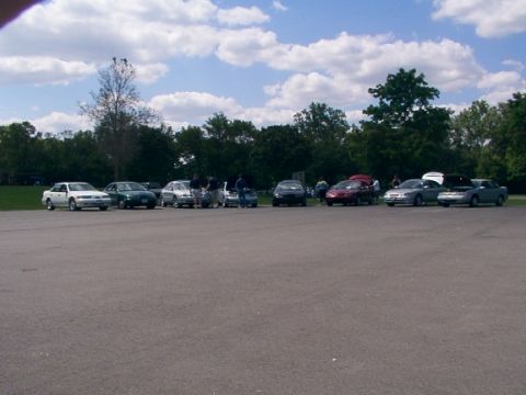 1998 Ford Taurus - A gathering of vehicles and people in an outdoor parking lot on a cloudy day.