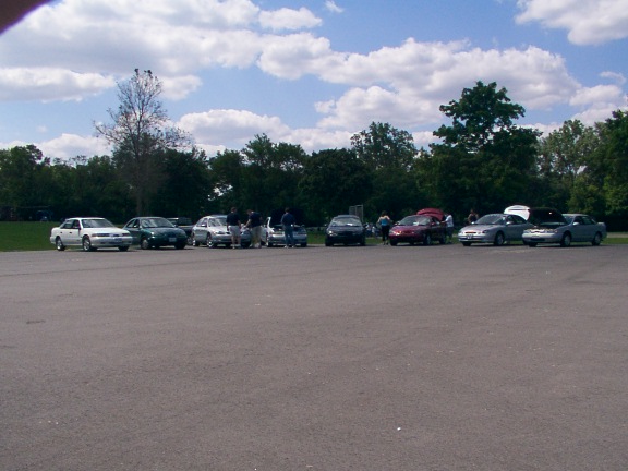 several cars parked in a lot with people standing around them