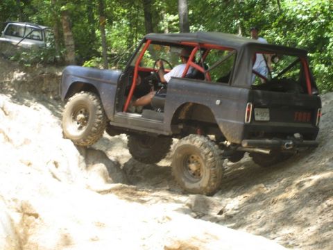 1995 Ford Bronco - This modified SUV, likely a 1970s Ford Bronco, navigates a challenging off-road course with another vehicle visible in the background.