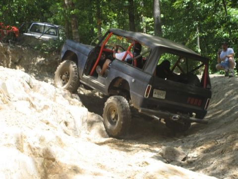 1995 Ford Bronco - A dark blue Ford Bronco with a red roll cage navigates a steep, rocky trail, while another vehicle waits behind.