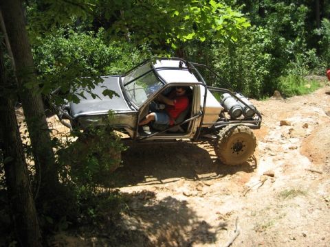 1995 Ford Bronco - A modified off-road vehicle navigates a rocky, wooded trail with a driver inside.