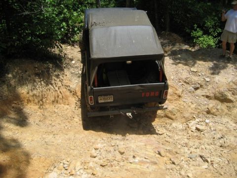 1995 Ford Bronco - A Ford pickup truck navigates a rocky, wooded trail with a person standing on the embankment watching.
