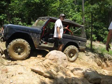 1995 Ford Bronco - A man stands in the open driver's door of a black off-road SUV navigating a rocky trail.