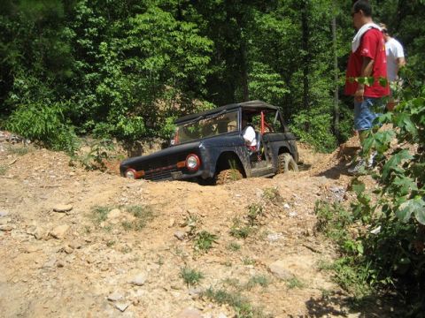 1995 Ford Bronco - A dark blue Ford Bronco is stuck in a dirt ditch with its front wheels submerged.