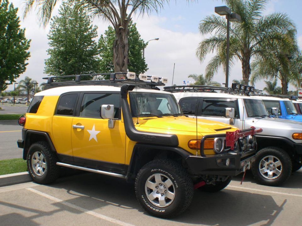 Yellow Toyota FJ Cruiser with snorkel and roof lights, parked next to other FJ Cruisers