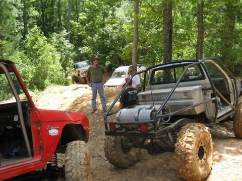 1995 Ford Bronco - A modified red 1995 Ford Bronco is parked on a dirt trail with other off-road vehicles and people.