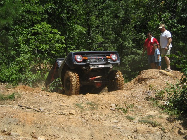 Ford Bronco climbing a steep dirt hill with two men and a child watching