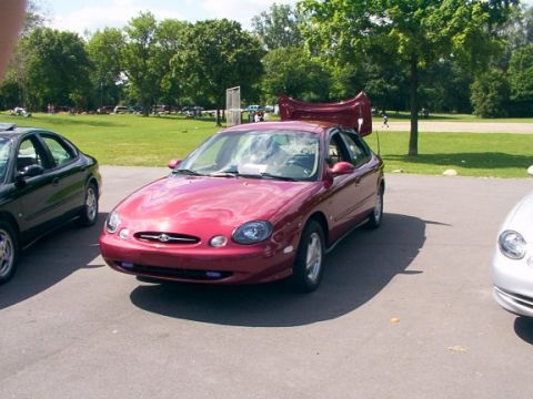 1998 Ford Taurus - A red 1998 Ford Taurus is parked with its hood open, alongside another vehicle.