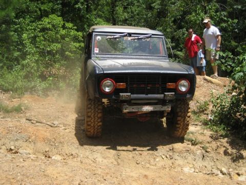 1995 Ford Bronco - A Ford Bronco navigates a dusty, wooded trail with two men watching.